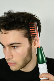 Uomo utilizza pettine elettrico per capelli su sfondo bianco. Strumento per cura capelli, styling maschile, tecnologia bellezza.