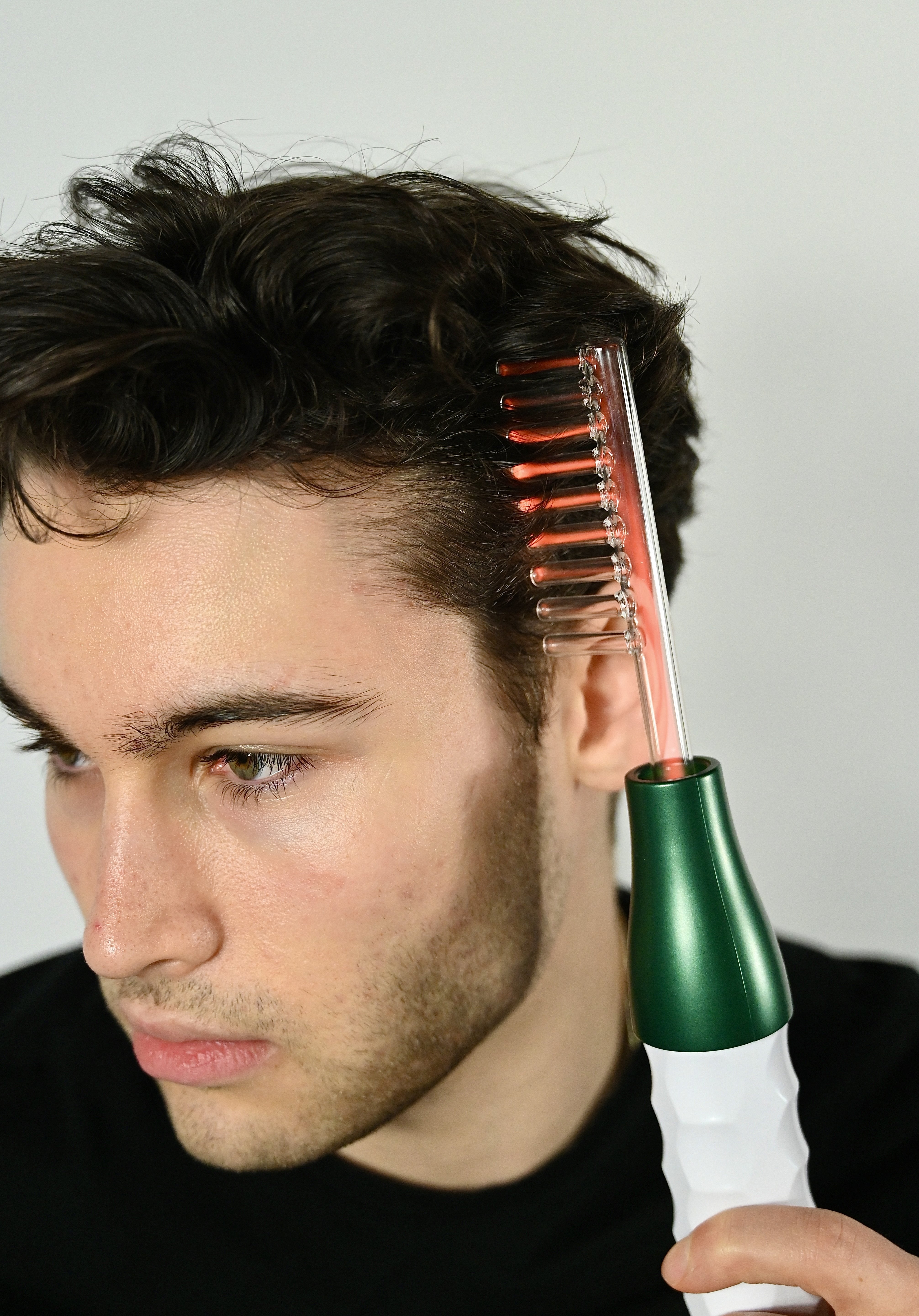 Uomo utilizza pettine elettrico per capelli su sfondo bianco. Strumento per cura capelli, styling maschile, tecnologia bellezza.