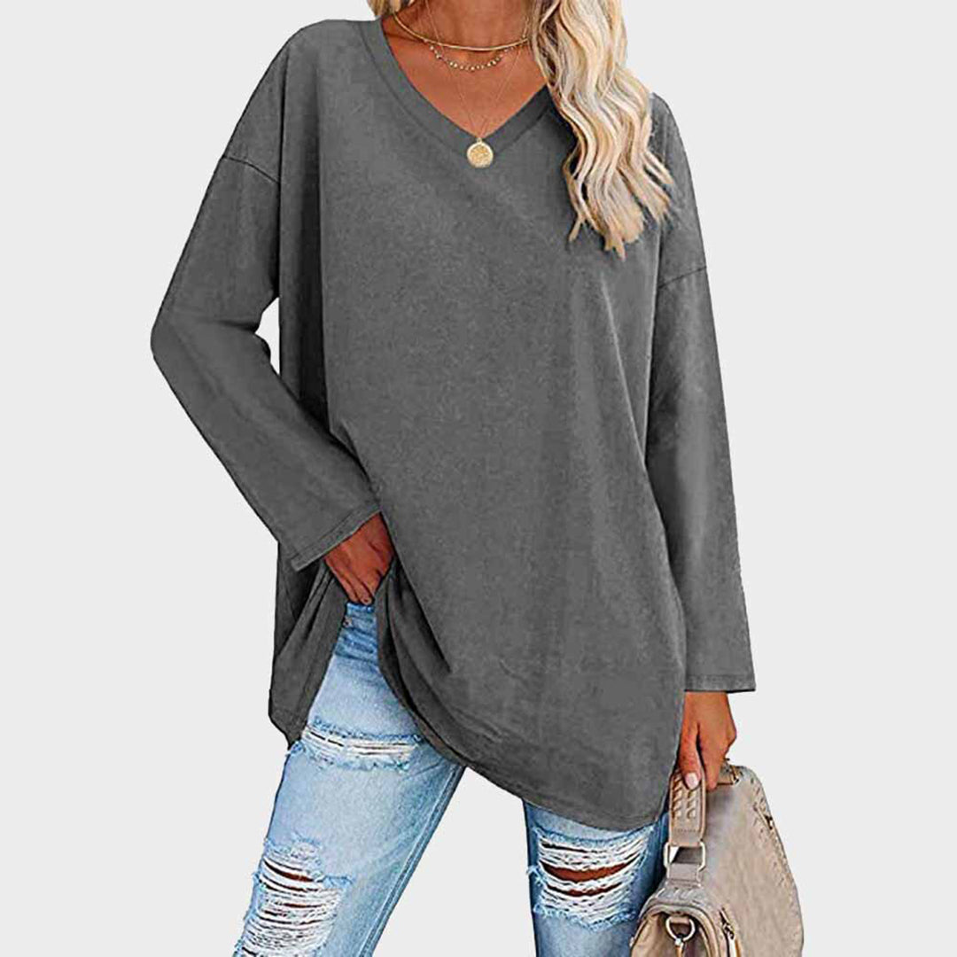 Maglia oversize grigia a maniche lunghe, scollo a V, indossata con jeans strappati. Look casual donna, moda autunnale, stile urbano.