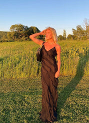 Donna in abito nero elegante in un campo al tramonto, con borsa a spalla. Moda estiva, abbigliamento femminile, natura, luce dorata.
