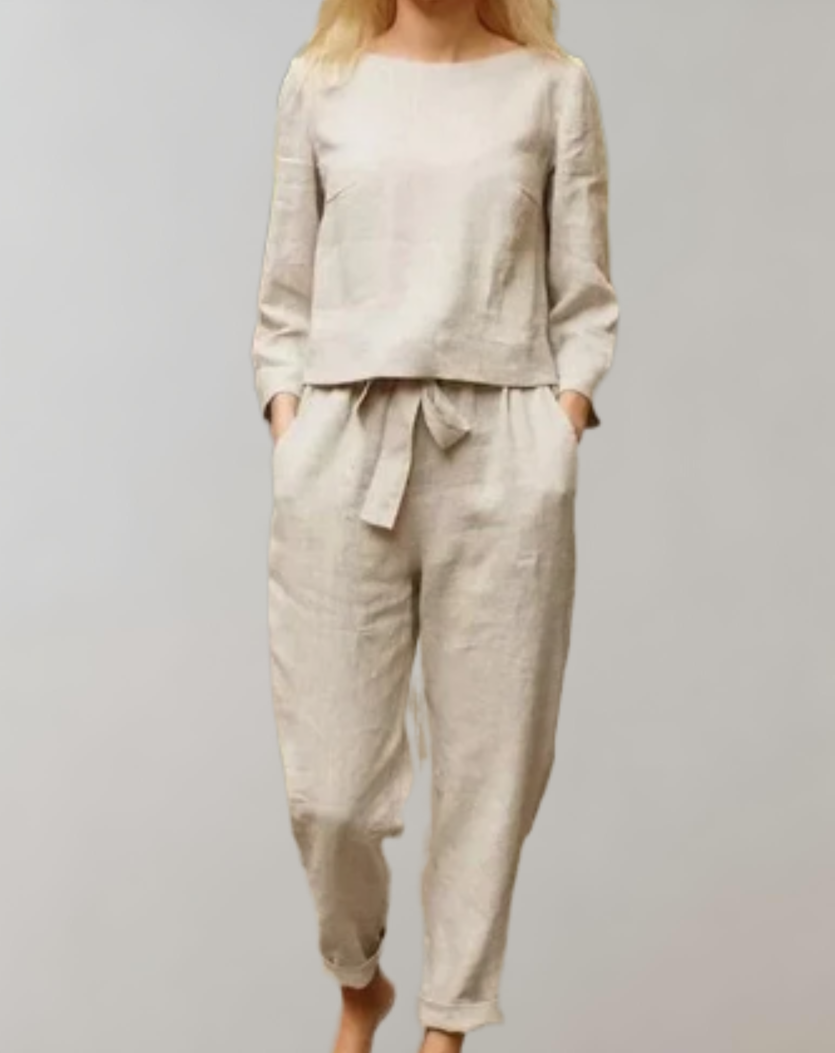 Donna in completo lino beige, composto da maglia a maniche lunghe e pantaloni con cintura. Abbigliamento casual elegante, moda sostenibile.