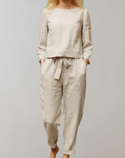 Donna in completo lino beige, composto da maglia a maniche lunghe e pantaloni con cintura. Abbigliamento casual elegante, moda sostenibile.