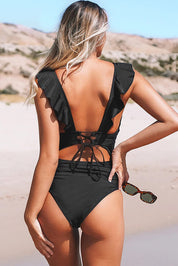 Donna in costume da bagno nero con volant sulla schiena, in spiaggia. Moda mare, estate, abbigliamento donna, costume intero elegante.