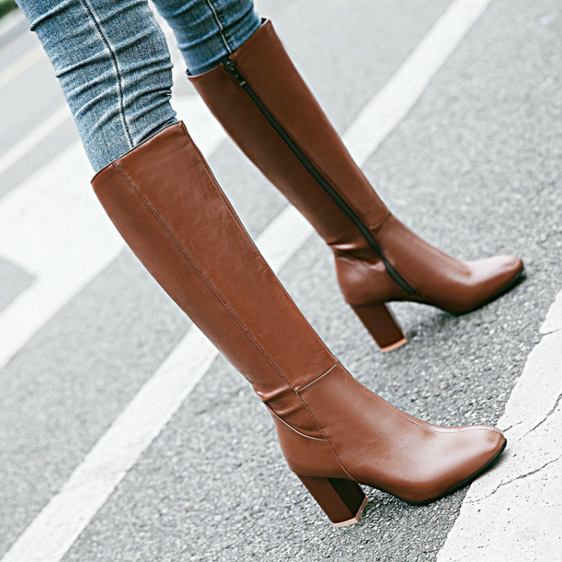Stivali alti marroni in pelle con tacco largo, chiusura a zip laterale, indossati su jeans. Scarpe moda donna autunno inverno.