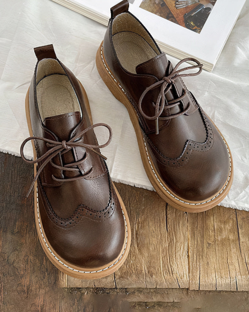 Scarpe stringate in pelle marrone scuro con suola in gomma beige, design brogue, su tavolo di legno. Scarpe eleganti uomo, moda autunno.