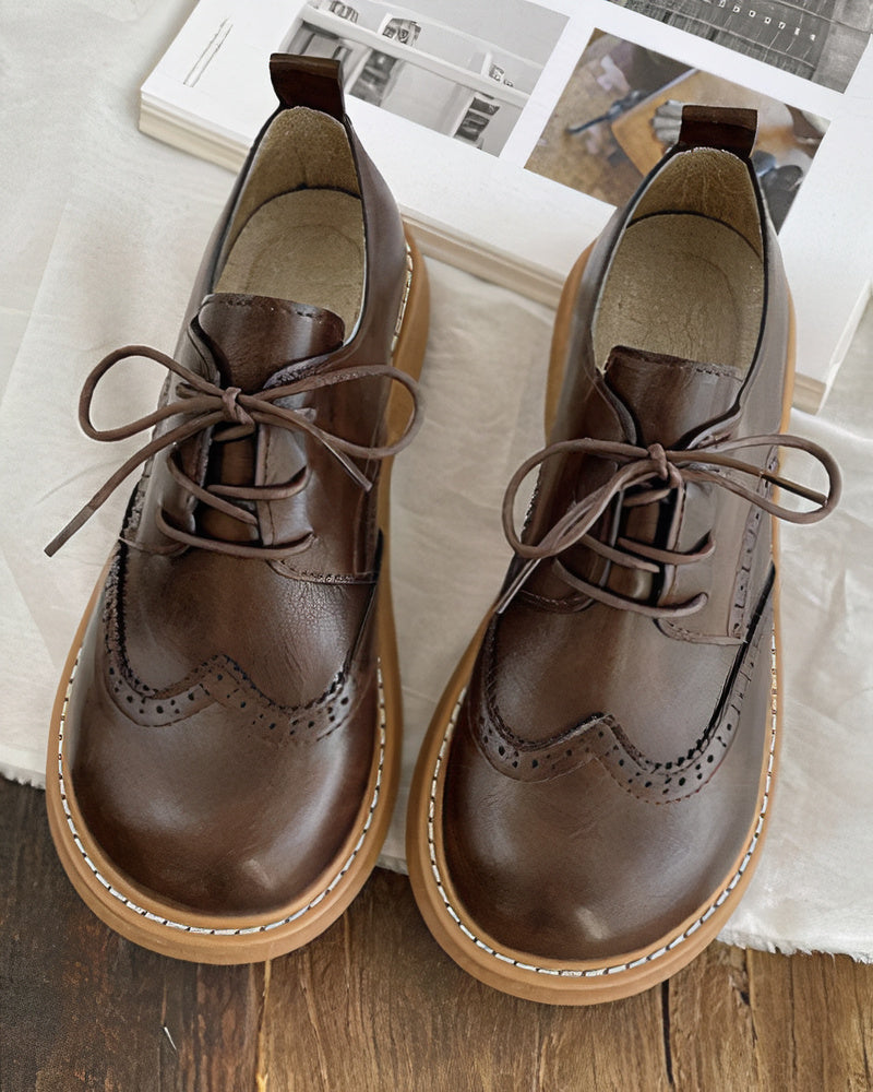 Scarpe stringate in pelle marrone con suola in gomma, design brogue, su sfondo di libri. Eleganti e versatili, ideali per look casual e formali.