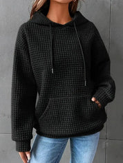 Felpa nera con cappuccio e tasca frontale, tessuto a trama waffle, indossata da una persona. Abbigliamento casual donna, moda autunno inverno.
