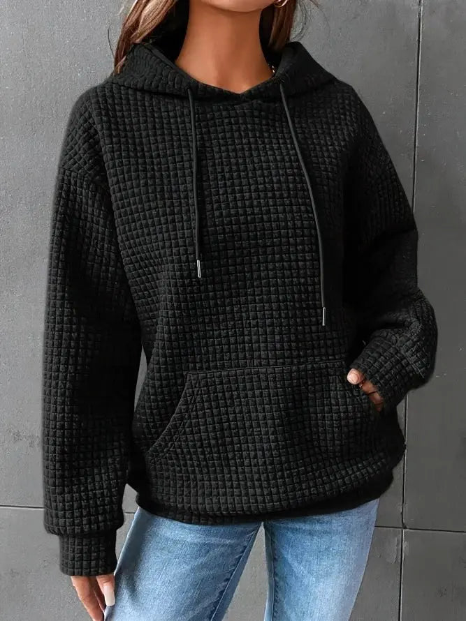 Felpa nera con cappuccio e tasca frontale, tessuto a trama waffle, indossata da una persona. Abbigliamento casual donna, moda autunno inverno.
