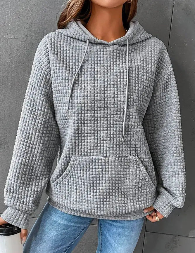 Felpa grigia a quadri con cappuccio, tasca frontale e maniche lunghe, indossata da una donna. Stile casual, ideale per l'autunno.