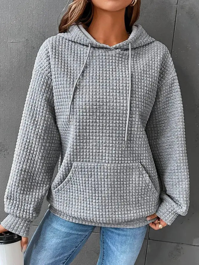 Felpa grigia a quadri con cappuccio, tasca frontale e maniche lunghe, indossata da una donna. Stile casual, ideale per l'autunno.