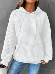 Felpa bianca con cappuccio in tessuto waffle, tasca frontale, indossata da una donna. Stile casual, ideale per l'autunno e l'inverno.
