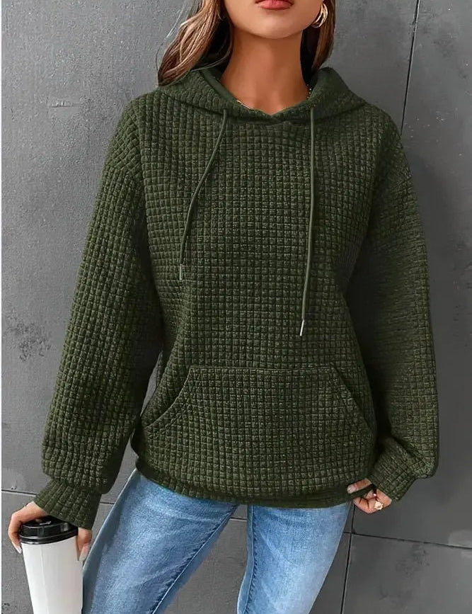Donna con felpa verde a coste, cappuccio e tasca frontale, tiene una tazza da viaggio. Indossa jeans blu. Moda casual autunnale.