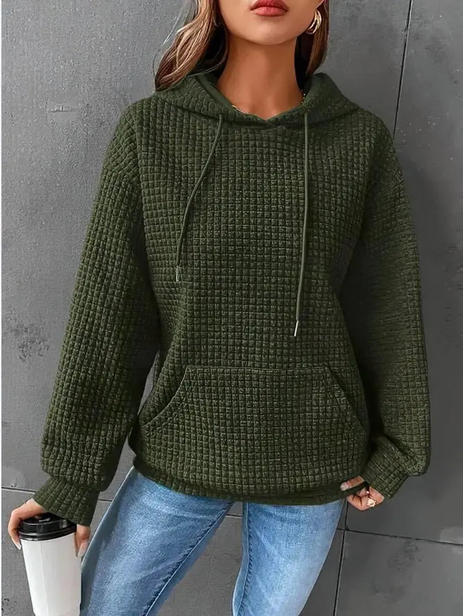 Donna con felpa verde a coste, cappuccio e tasca frontale, tiene una tazza da viaggio. Indossa jeans blu. Moda casual autunnale.