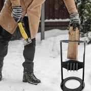Uomo spacca legna con ascia gialla in giardino innevato, indossa cappotto beige e guanti a righe. Spaccalegna nero in primo piano.