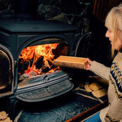 Donna accende stufa a legna in ghisa, camino acceso, legna ardente, riscaldamento domestico, ambiente accogliente, inverno, calore naturale.