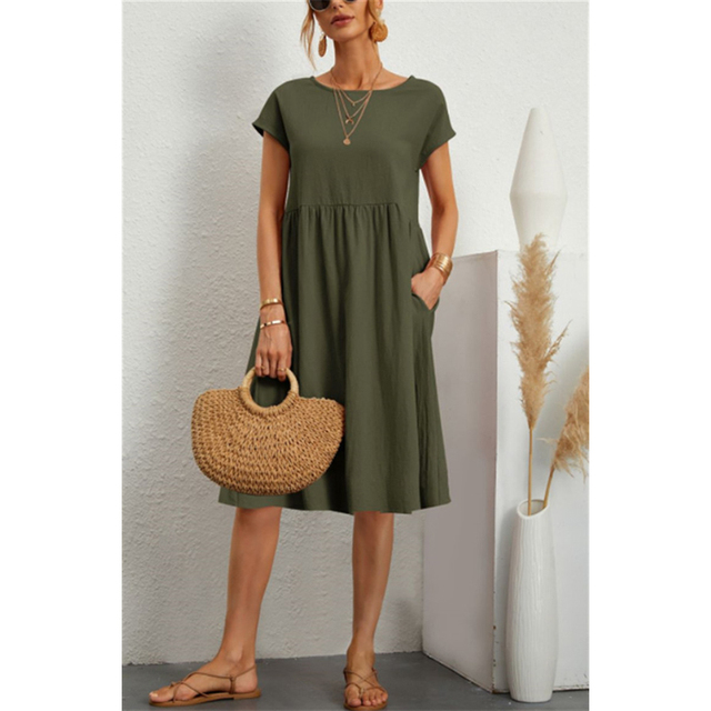 Abito estivo verde oliva da donna, maniche corte, lunghezza al ginocchio, con tasche. Accessori: borsa paglia, sandali, gioielli dorati.