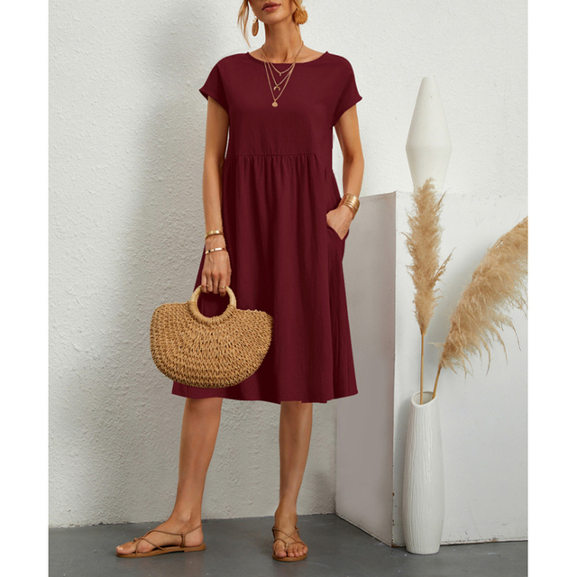 Abito midi rosso bordeaux, maniche corte, con collana dorata e borsa in paglia. Look estivo elegante, perfetto per occasioni casual.