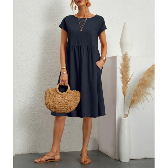 Abito estivo donna blu scuro, maniche corte, con borsa paglia intrecciata e sandali. Look casual elegante, moda femminile estiva.