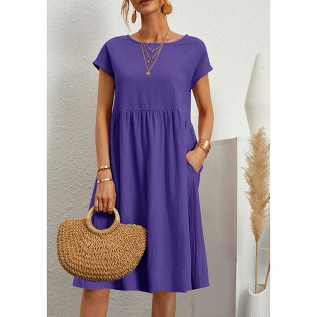Abito estivo viola donna, maniche corte, con tasche. Accessori: collane dorate, borsa paglia. Moda casual elegante. Sfondo neutro.