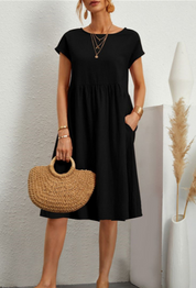 Abito nero estivo donna, maniche corte, lunghezza al ginocchio, con borsa paglia intrecciata. Look casual elegante, moda femminile 2023.