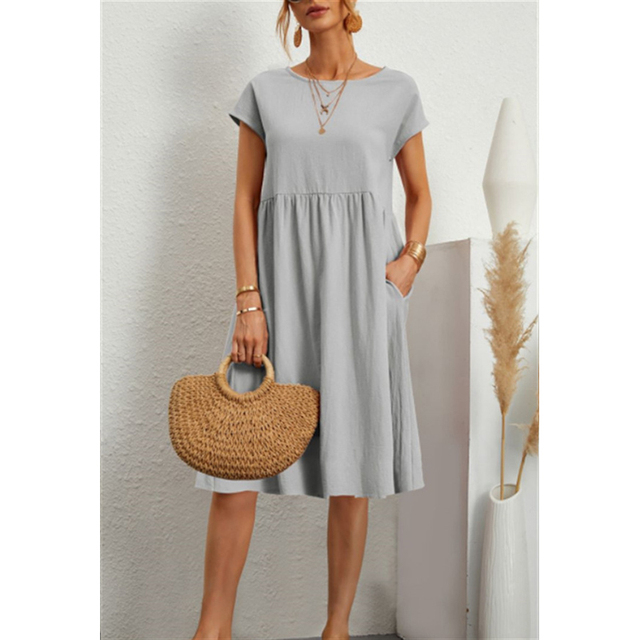 Abito estivo donna grigio chiaro, maniche corte, con tasche. Accessori: borsa paglia, collana oro. Moda casual elegante.