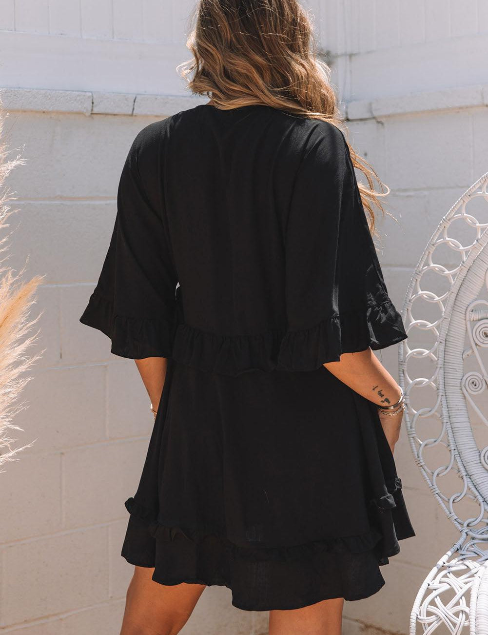 Donna con abito nero estivo, maniche a tre quarti, volant, in giardino. Moda femminile, abbigliamento casual elegante, tendenze estive.