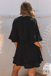 Donna con abito nero estivo, maniche a tre quarti, volant, in giardino. Moda femminile, abbigliamento casual elegante, tendenze estive.