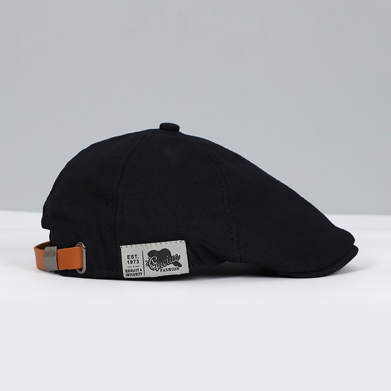 Cappello piatto nero in cotone con cinturino regolabile in pelle marrone, etichetta laterale, stile vintage, moda uomo, accessorio elegante.