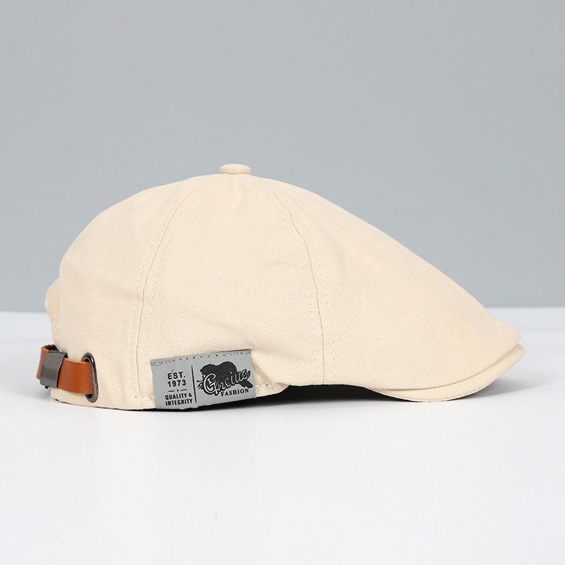 Cappello piatto beige in cotone con cinturino regolabile in pelle marrone, etichetta "Quality Fashion". Elegante accessorio moda uomo.