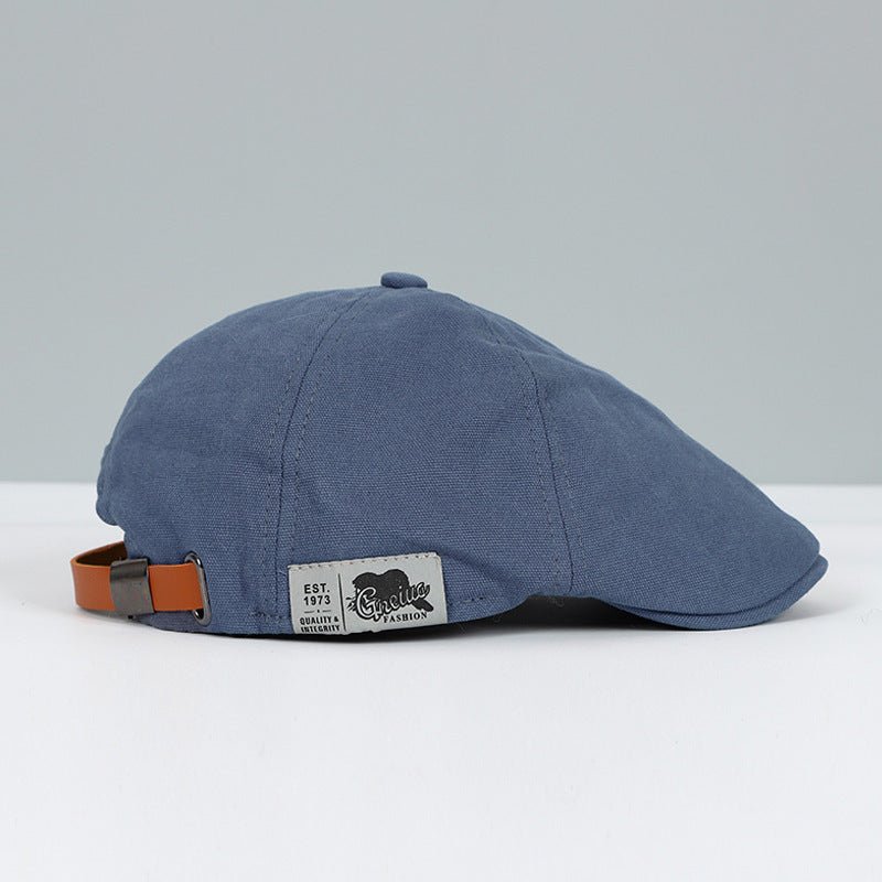Cappello piatto blu in cotone con cinturino regolabile in pelle marrone, etichetta "Genuine Fashion". Accessorio moda uomo elegante e casual.
