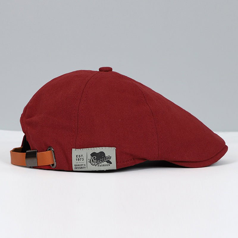 Cappello piatto uomo in cotone rosso, stile vintage, con cinturino regolabile in pelle marrone e etichetta laterale. Accessorio moda elegante.