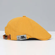 Cappello piatto giallo senape in cotone, stile vintage, con cinturino regolabile in pelle marrone. Accessorio moda unisex elegante e casual.
