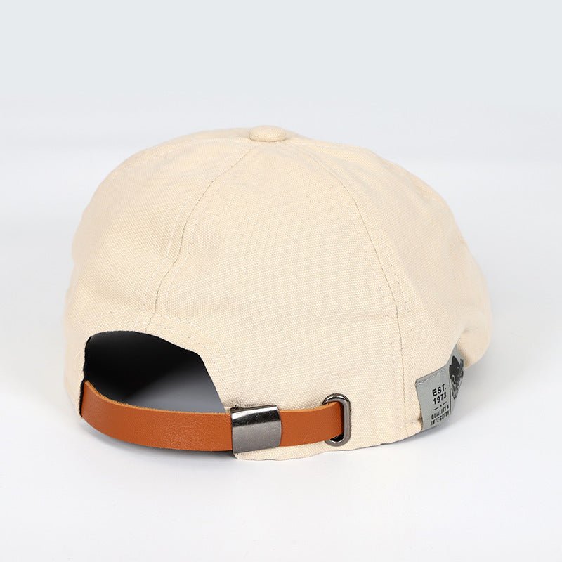 Berretto beige in cotone con cinturino regolabile in pelle marrone, stile casual, unisex. Accessorio moda versatile per tutte le stagioni.
