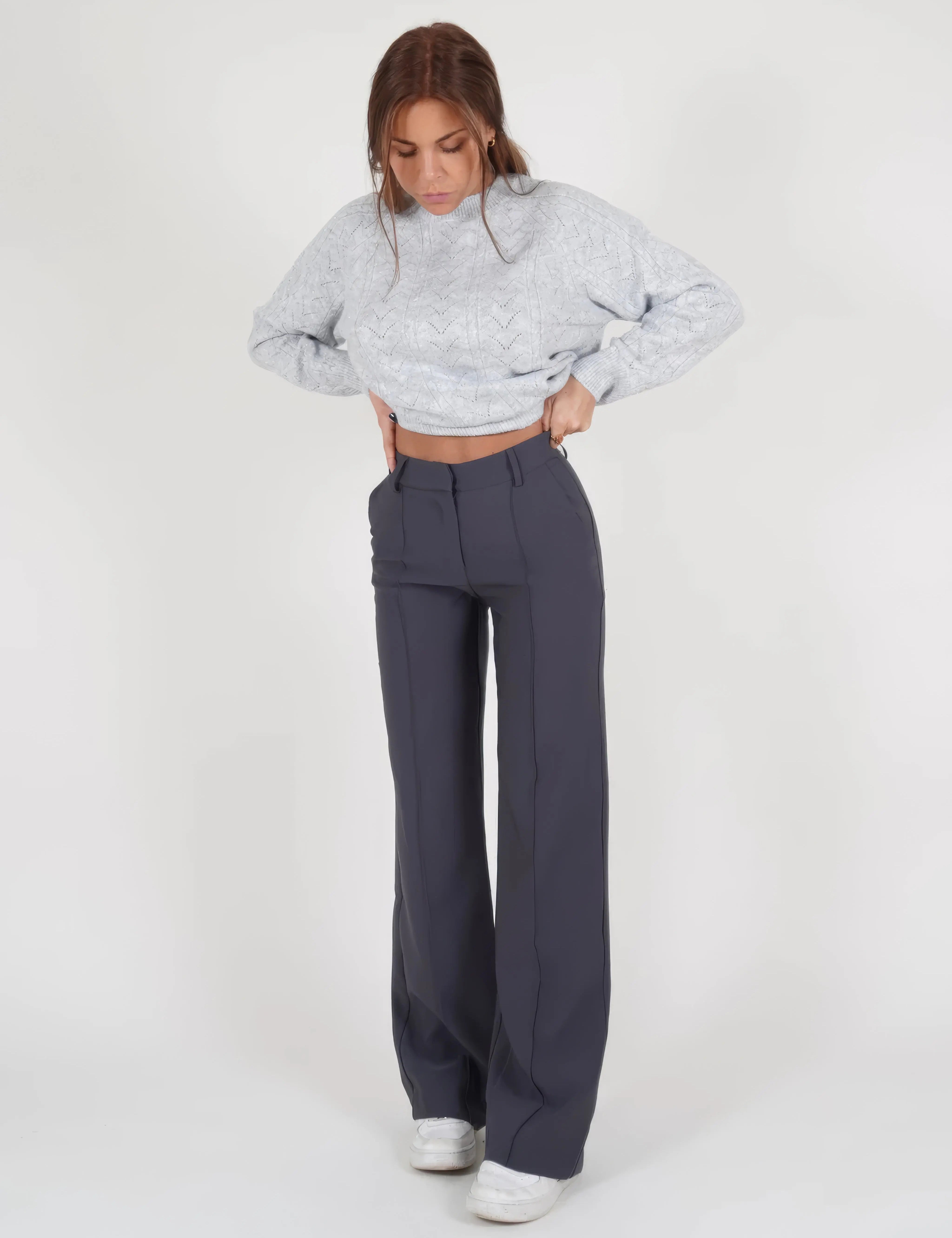 Donna con maglione grigio lavorato a maglia e pantaloni blu scuro a vita alta, scarpe bianche. Moda casual autunnale, abbigliamento femminile elegante.
