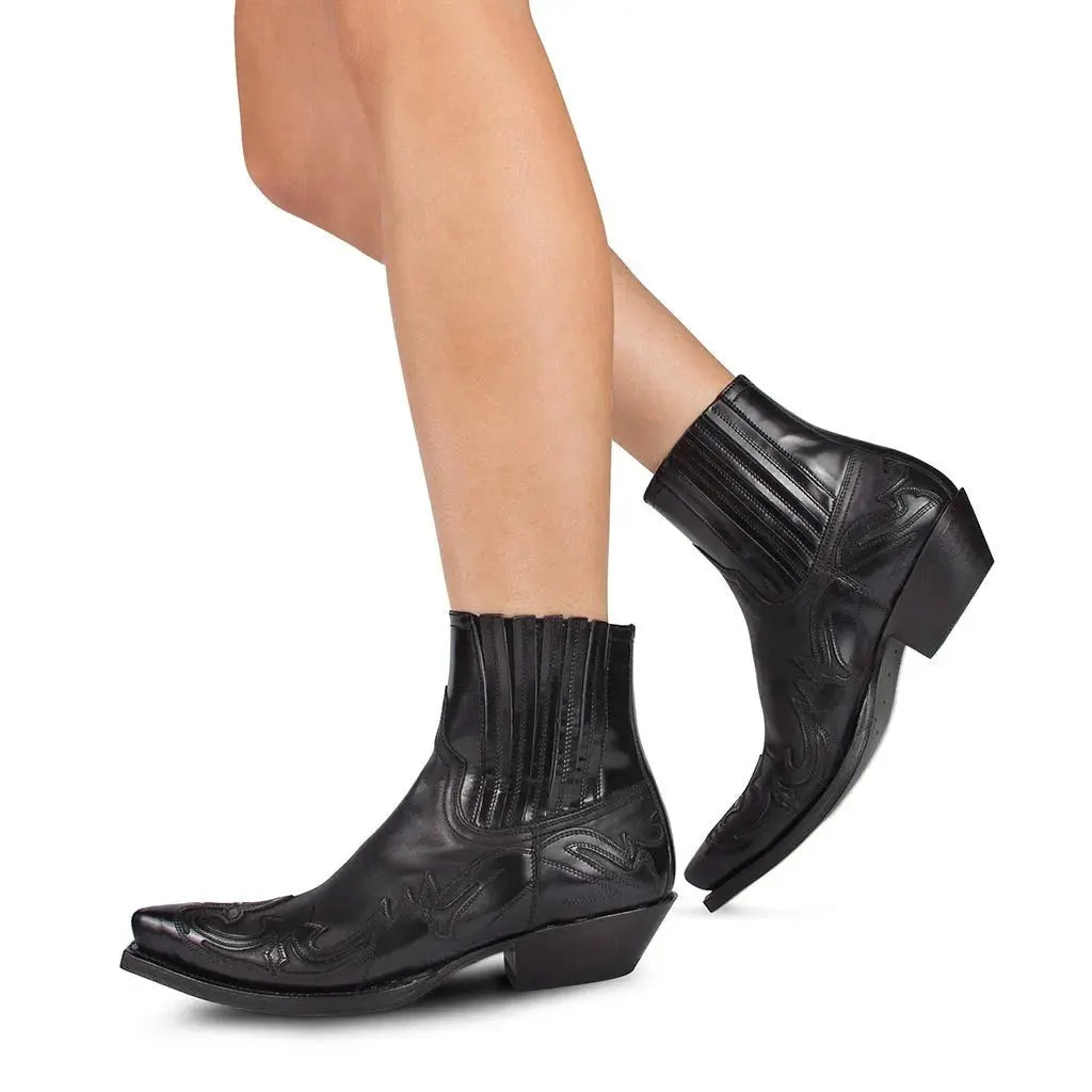 Stivaletti texani neri in pelle con tacco basso e dettagli ricamati, indossati su gambe femminili. Scarpe western eleganti e alla moda.