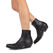 Stivaletti texani neri in pelle con tacco basso e dettagli ricamati, indossati su gambe femminili. Scarpe western eleganti e alla moda.