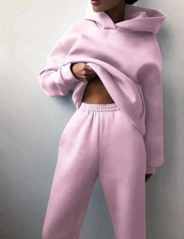 Donna in tuta sportiva rosa pastello, felpa con cappuccio e pantaloni comodi. Abbigliamento casual, moda donna, stile rilassato.