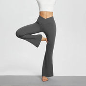 Donna in posa yoga con pantaloni a zampa grigi e top bianco. Abbigliamento sportivo, moda fitness, pantaloni yoga comodi ed eleganti.