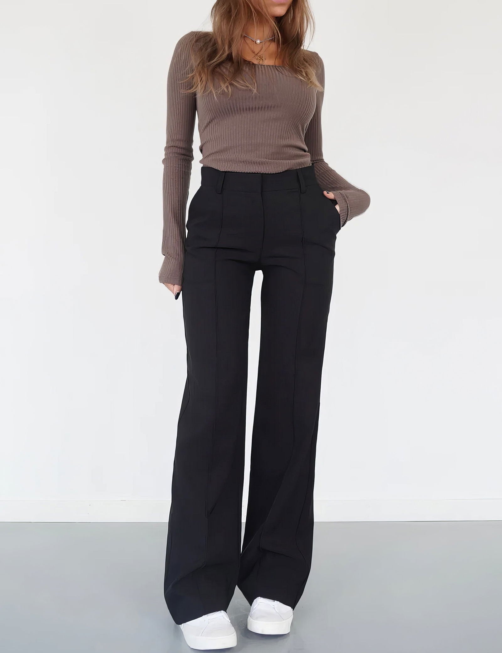 Donna in maglia marrone e pantaloni neri a zampa, scarpe bianche. Moda casual autunnale, abbigliamento femminile elegante e confortevole.
