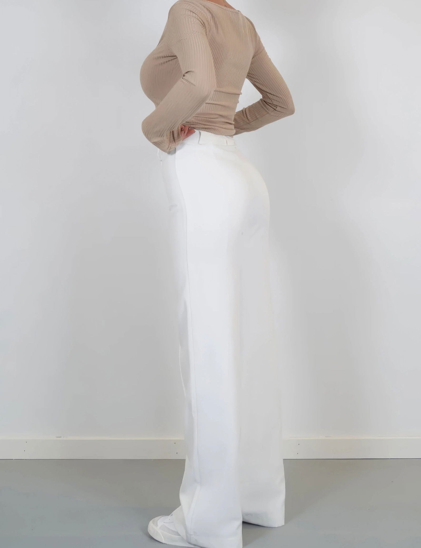 Pantaloni bianchi a vita alta da donna, taglio ampio, abbinati a maglia beige a maniche lunghe. Stile elegante e moderno, perfetto per ogni occasione.