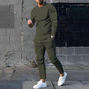 Uomo con completo sportivo verde oliva, maglia a maniche lunghe e pantaloni abbinati, indossa occhiali da sole e scarpe bianche, sfondo urbano.