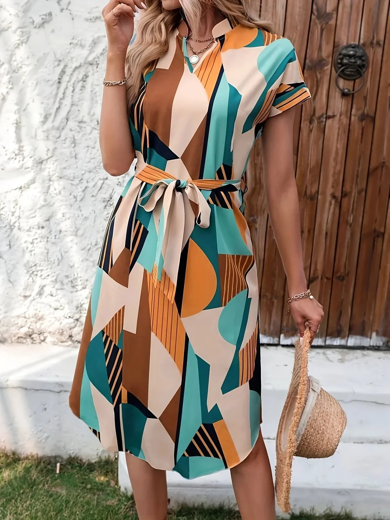 Abito estivo donna a maniche corte con stampa geometrica multicolore, cintura in vita, sfondo esterno, moda casual elegante.