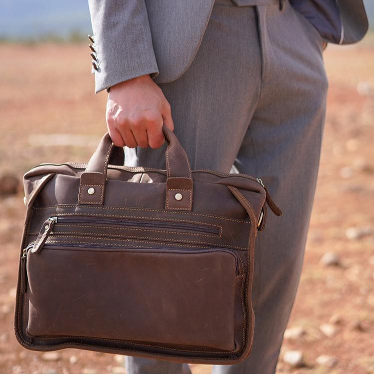 Uomo in abito grigio con borsa ventiquattrore in pelle marrone, elegante e professionale, ideale per lavoro e ufficio.