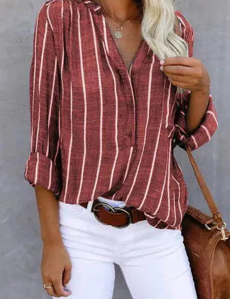 Camicia a righe verticali rosse e bianche, maniche lunghe, abbinata a pantaloni bianchi e cintura marrone. Stile casual elegante per donna.