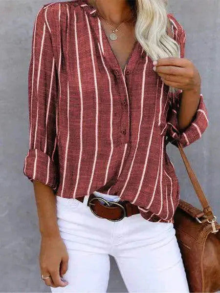 Camicia a righe verticali rosse e bianche, maniche lunghe, abbinata a pantaloni bianchi e cintura marrone. Stile casual elegante per donna.