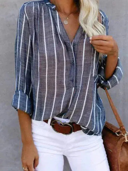 Camicia a righe verticali blu e bianche da donna, maniche lunghe, abbinata a pantaloni bianchi e cintura marrone. Stile casual elegante.