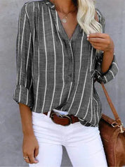 Camicia a righe verticali grigie e bianche, maniche lunghe, abbinata a pantaloni bianchi e borsa marrone. Moda casual donna, stile elegante.