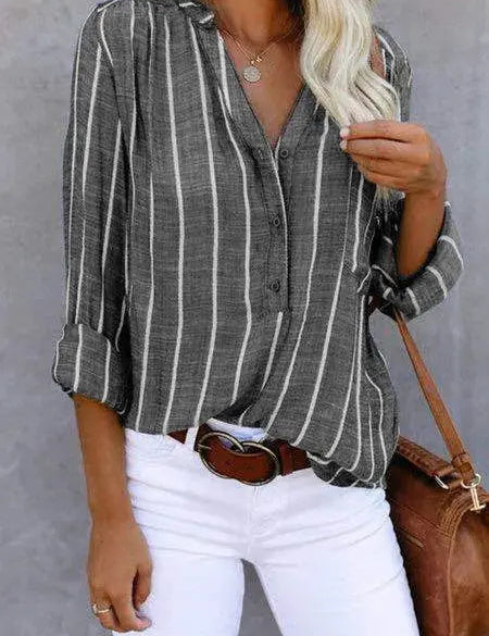 Camicia a righe verticali grigie e bianche, maniche lunghe, abbinata a pantaloni bianchi e borsa marrone. Moda casual donna, stile elegante.