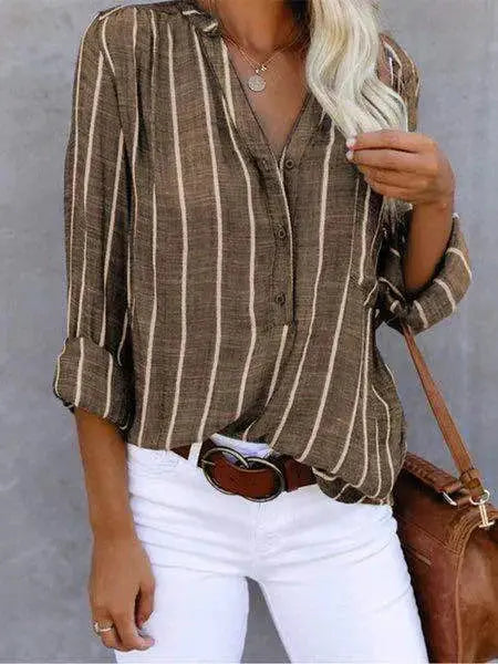 Camicia a righe verticali marrone e bianca, maniche lunghe, abbinata a pantaloni bianchi. Stile casual elegante, moda donna autunnale.