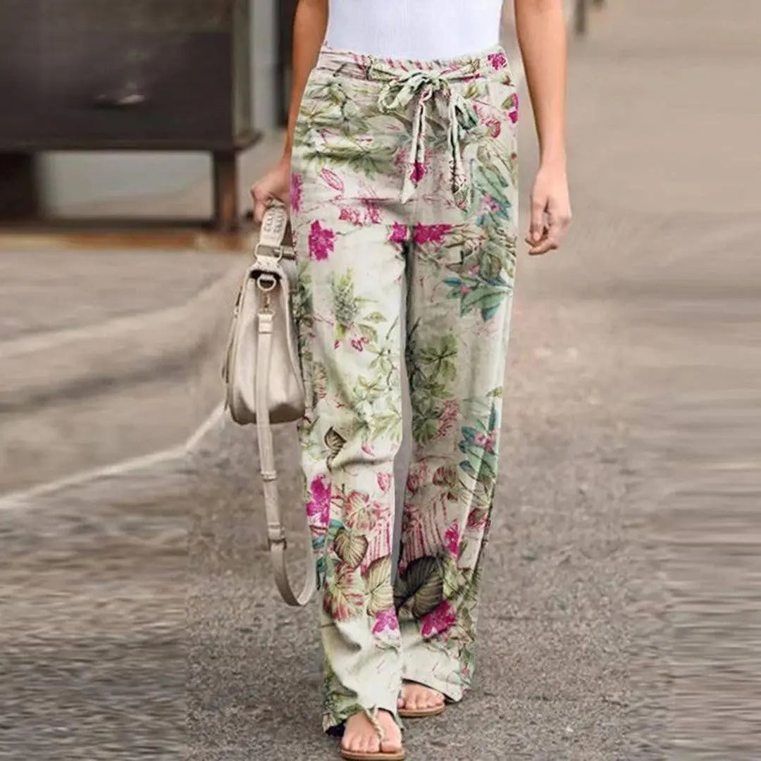 Pantaloni larghi donna floreali, vita alta con laccio, tessuto leggero, perfetti per estate, moda casual, abbinati a top bianco e borsa beige.